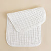A stack of three white quilted muslin burp cloths resting on a light beige surface.