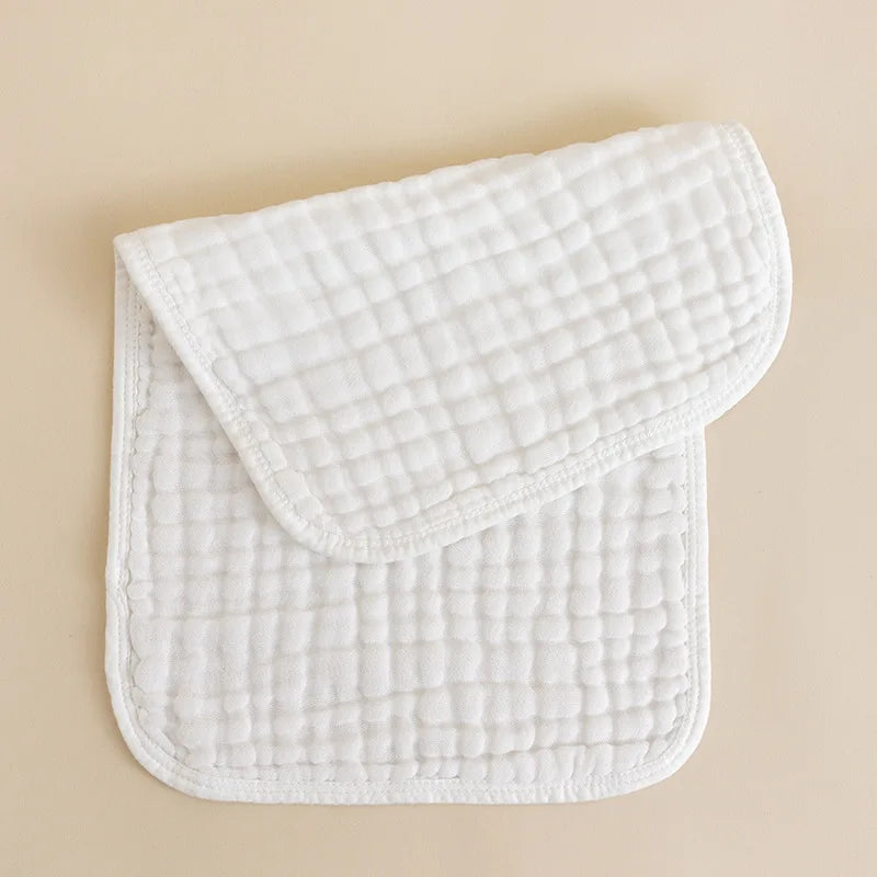 A stack of three white quilted muslin burp cloths resting on a light beige surface.