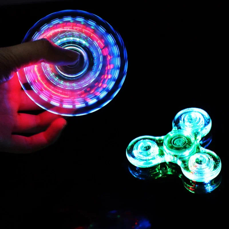A hand spins a glowing LED fidget spinner, creating colorful light patterns against a dark background.
