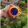 An orange retractable clothesline with a blue handle and wooden clothespins is held in a hand against a blurred green outdoor