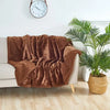 A brown faux fur throw blanket draped over a white sofa next to a large potted palm plant.