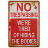 A vintage metal tin sign with red and white text that reads NO TRESPASSING WE'RE TIRED OF HIDING THE BODIES