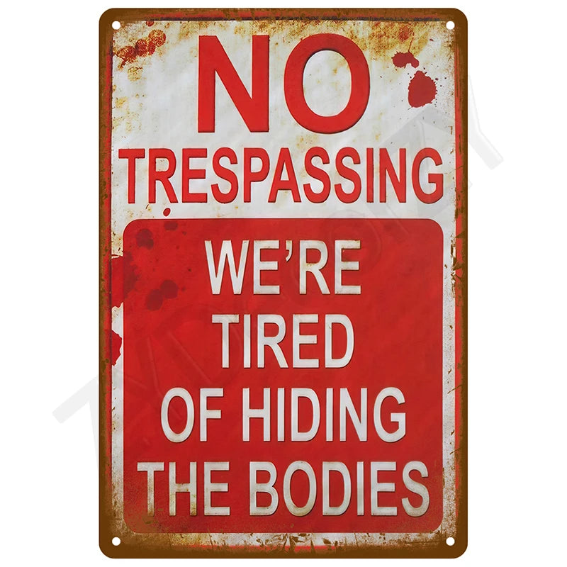 A vintage metal tin sign with red and white text that reads NO TRESPASSING WE'RE TIRED OF HIDING THE BODIES