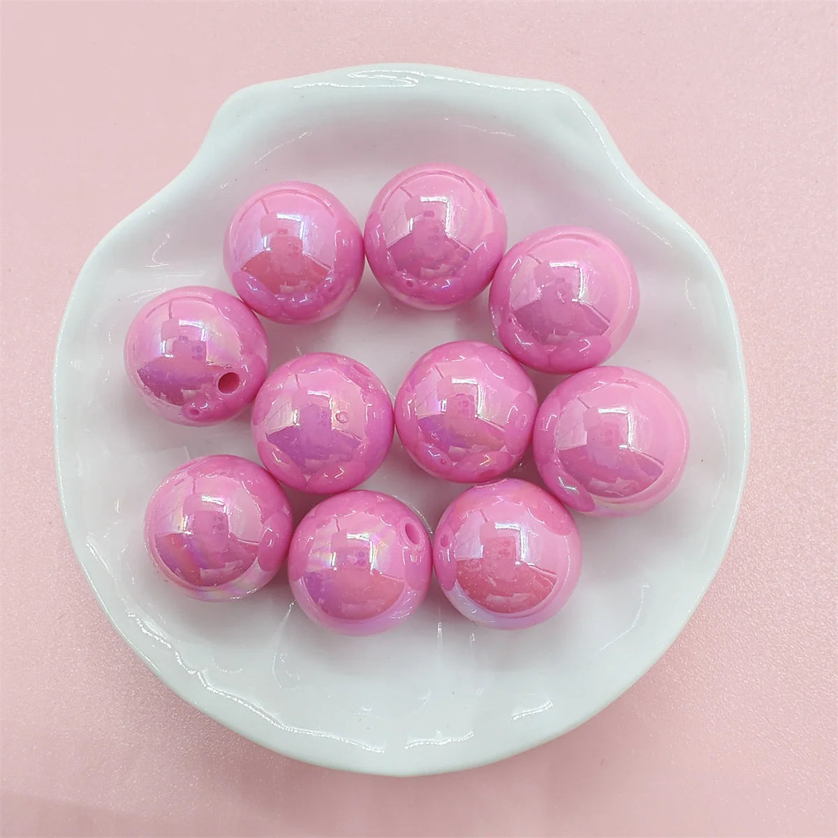A white oval dish holds ten glossy pink acrylic beads for jewelry making.