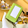 A hand holds a lime green compact wallet with a clear window and a black strap against a blurred background of toys.