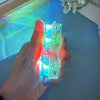 A hand holds a clear LED light-up keyboard keychain fidget toy, illuminating with bright blue and green light.