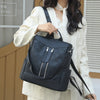 A woman is holding a black anti-theft leather backpack with silver zippers and a patterned design.