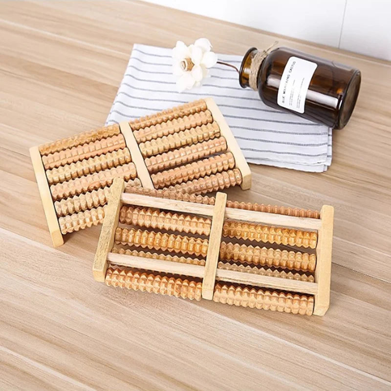 Wooden foot massage rollers for reflexology and tension relief placed on a wooden surface next to a glass bottle.