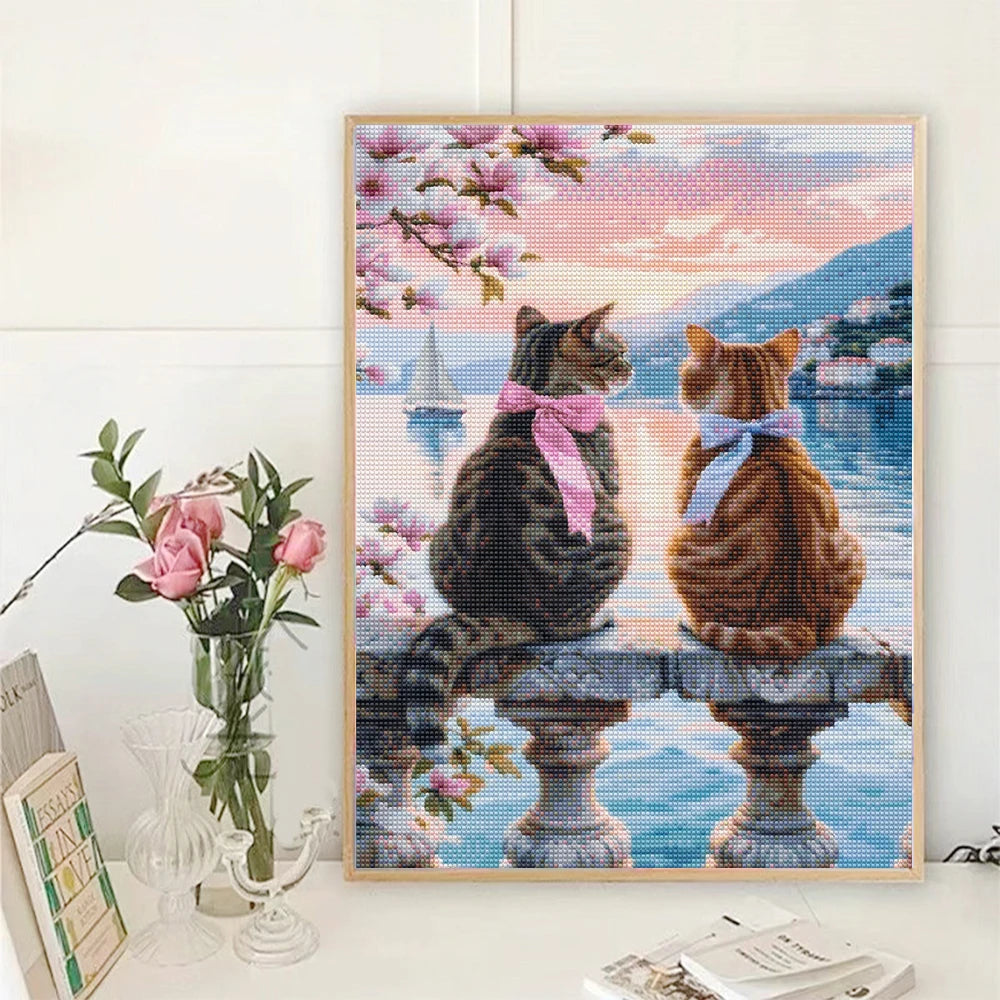 A diamond painting featuring two orange tabby cats sitting on a stone pedestal with pink and purple flowers.
