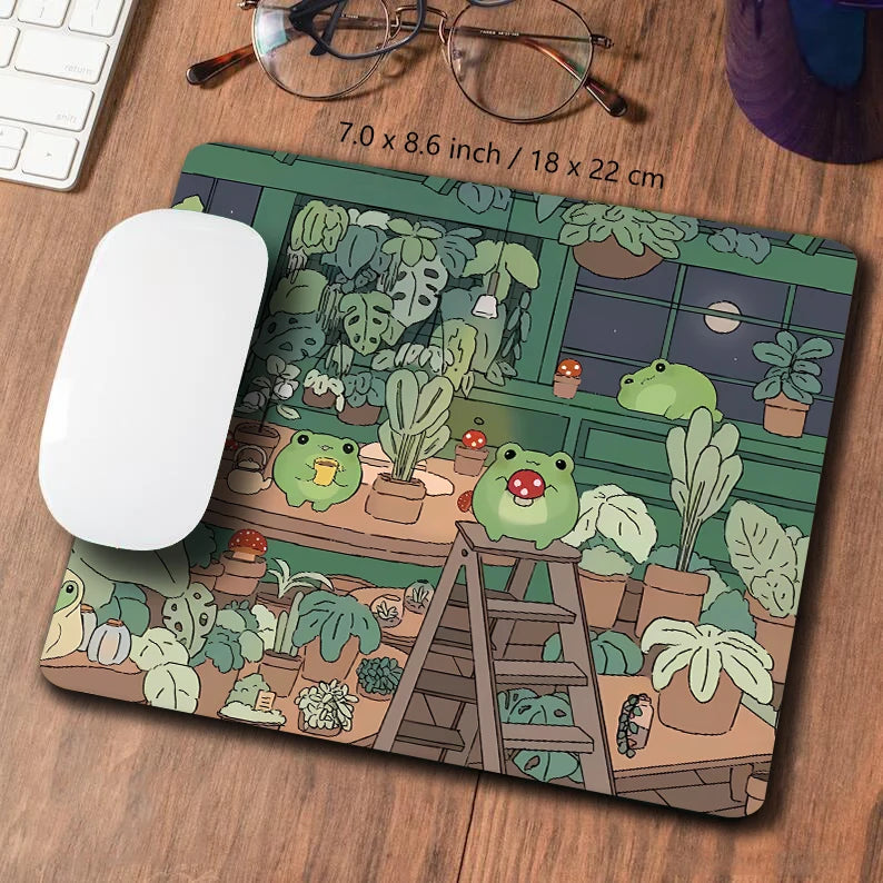 A large extended mousepad featuring a kawaii nature design of frogs and plants on a wooden desk.