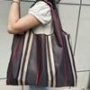 A person is holding a dark brown and beige striped foldable oxford cloth tote bag against a light gray background.