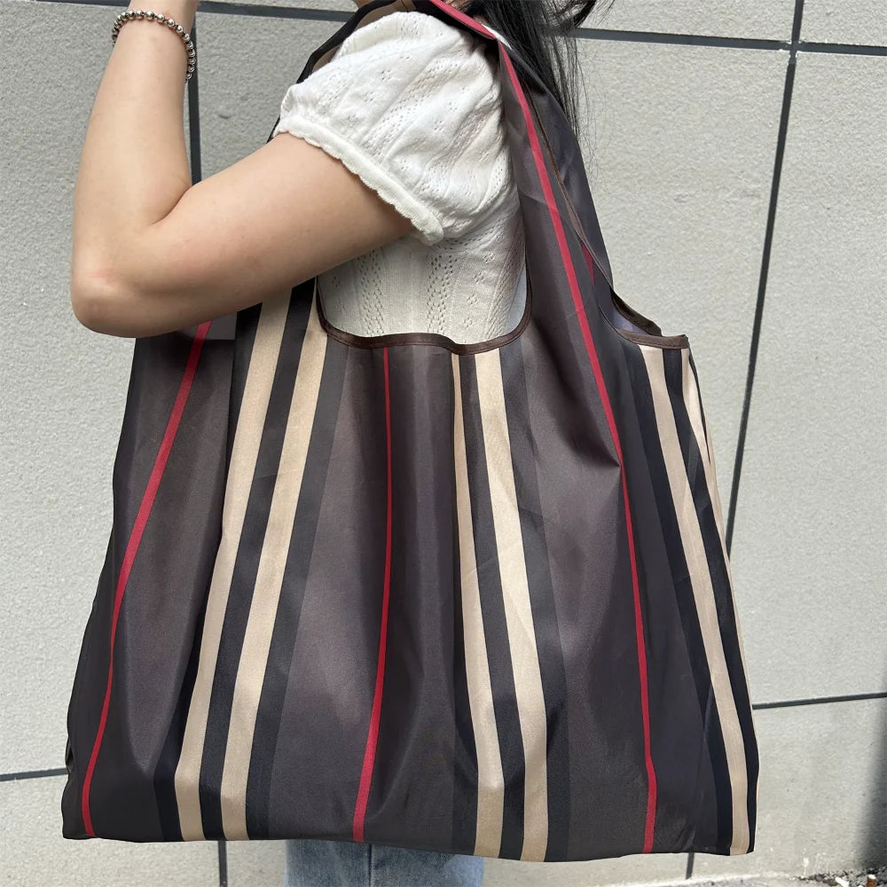 A person is holding a dark brown and beige striped foldable oxford cloth tote bag against a light gray background.