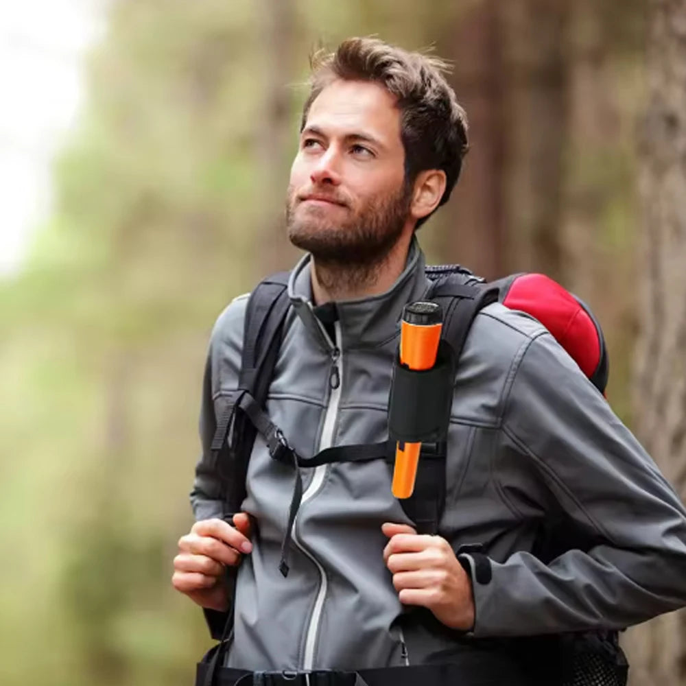 A man wearing a gray jacket and backpack is looking up outdoors while holding a handheld metal detector.