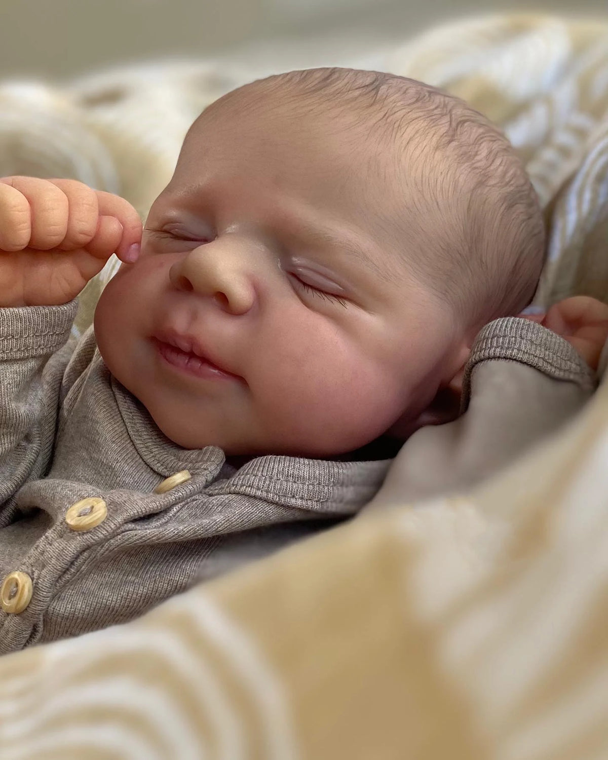 A close-up photo of a newborn baby doll with closed eyes resting on a soft, patterned fabric.