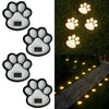 A set of four solar dog paw pathway lights illuminating a stone walkway in a garden.