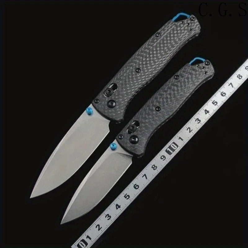 A silver carbon fiber folding knife with a black handle is shown next to a ruler for scale.