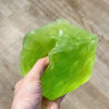 A hand holds a translucent, light green frosted matte jumbo cheese stress ball against a neutral background.