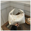 Cremfarbener Seidertasche mit zarten Perlenstickereien auf Holzoberfläche.