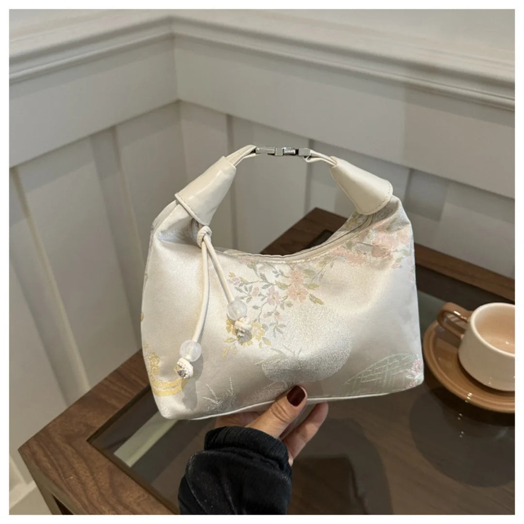 Cremfarbener Seidertasche mit zarten Perlenstickereien auf Holzoberfläche.