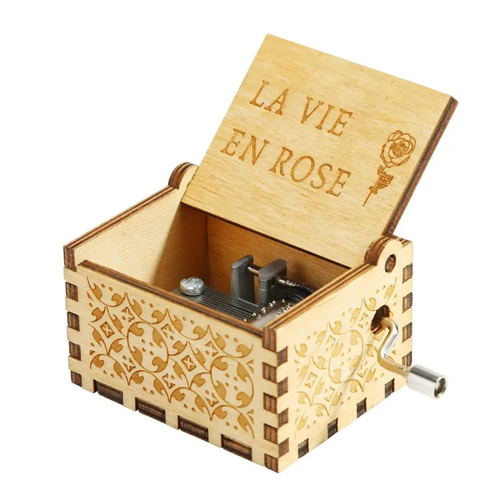 A light wood hand-cranked music box with a lid engraved 'La vie en rose' and decorative patterns.