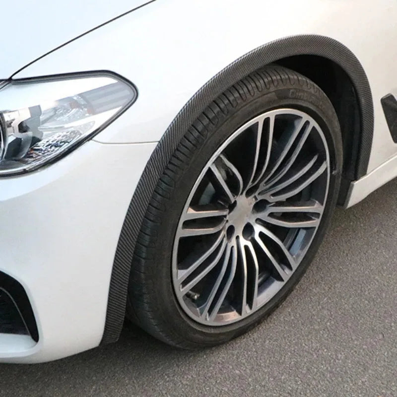 Close-up of a white car's front wheel showing carbon fiber wheel arch trim strips and alloy wheel.