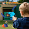 A young boy is aiming a blue foam dart blaster toy at targets set up on the grass.