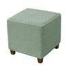 A square ottoman slipcover in a muted sage green color with a diamond lattice pattern.