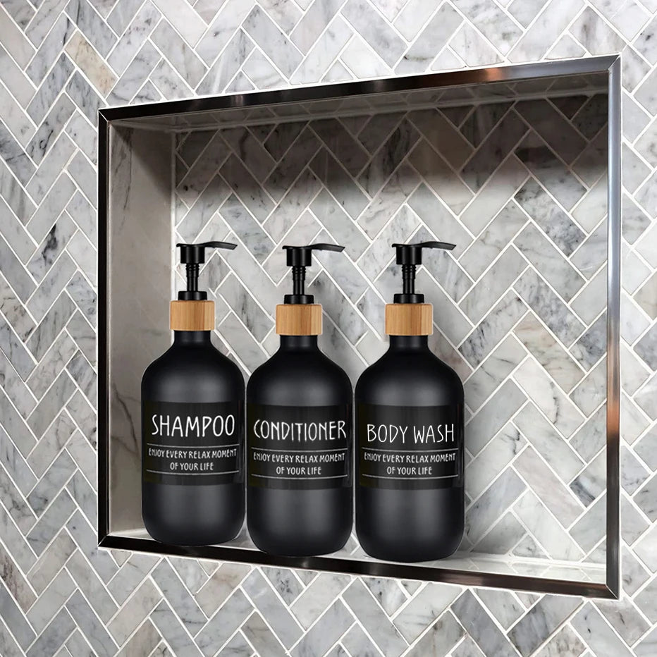 Three black refillable soap dispenser bottles for shampoo, conditioner, and body wash displayed in a modern bathroom shelf.
