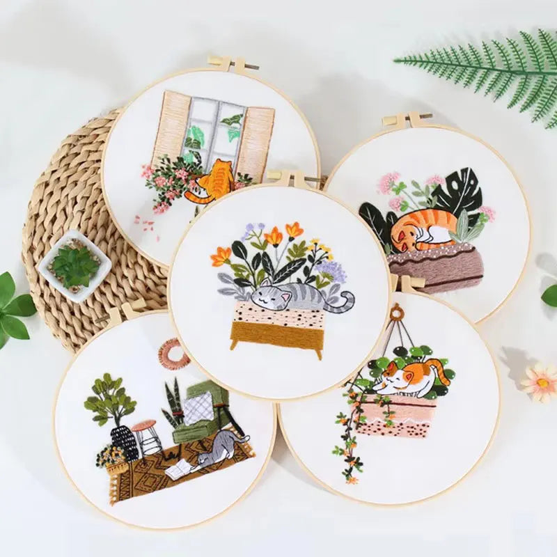 A collection of round embroidery hoops featuring floral and cat designs on white fabric.