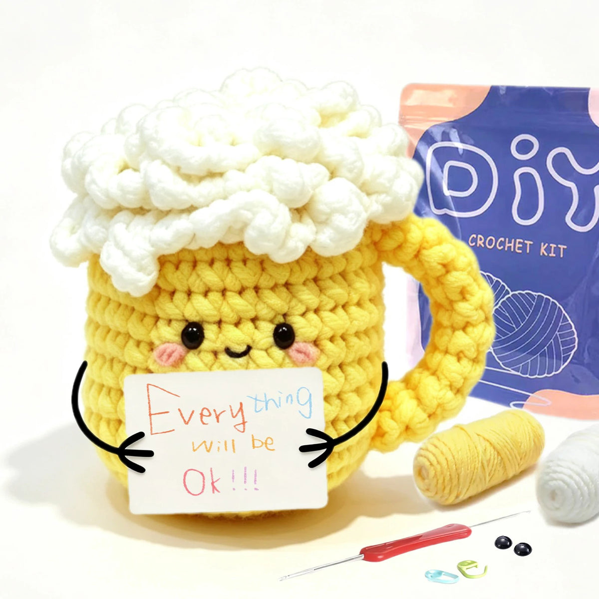 A yellow crocheted animal mug with pink accents sits next to yarn and a crochet kit.