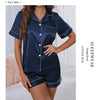 A woman models a navy blue satin pajama set consisting of a button-down top and matching shorts.