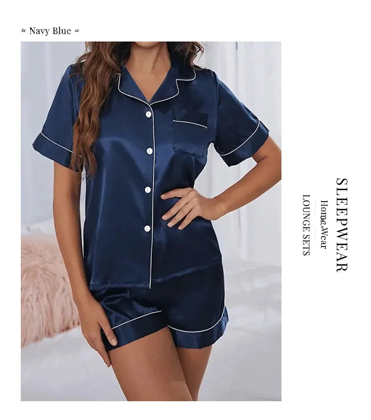 A woman models a navy blue satin pajama set consisting of a button-down top and matching shorts.