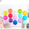 A collection of colorful round paper lanterns in shades of orange, green, pink, and blue hanging on a white wall.