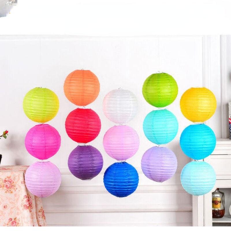 A collection of colorful round paper lanterns in shades of orange, green, pink, and blue hanging on a white wall.