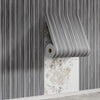 Vertical striped wallpaper sample showing a roll of wood grain peel-and-stick wall tiles mounted on a white wall.