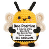 A yellow bee crochet figurine with black antennae and fuzzy wings, featuring an inspirational message card.
