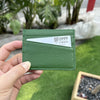 A hand holds a green leather slim card holder wallet with a white tag displaying the number 0999.