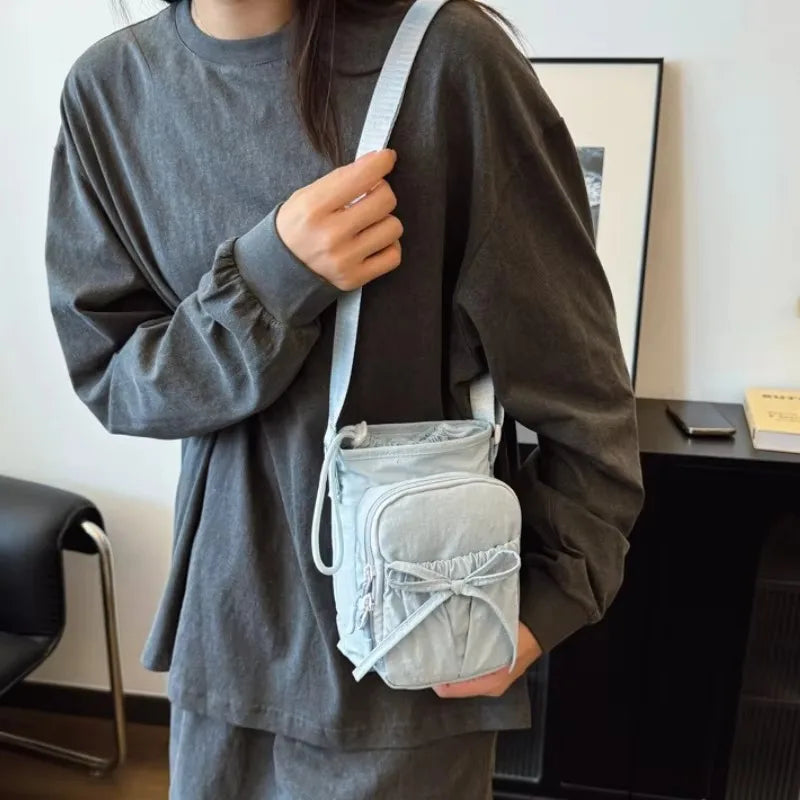 A person wearing a gray long-sleeved shirt holds a light blue bow-decorated casual crossbody bag.