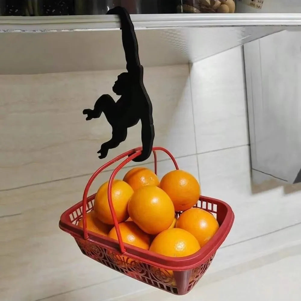 A black monkey-shaped wooden wall hook is hanging above a red basket filled with oranges.