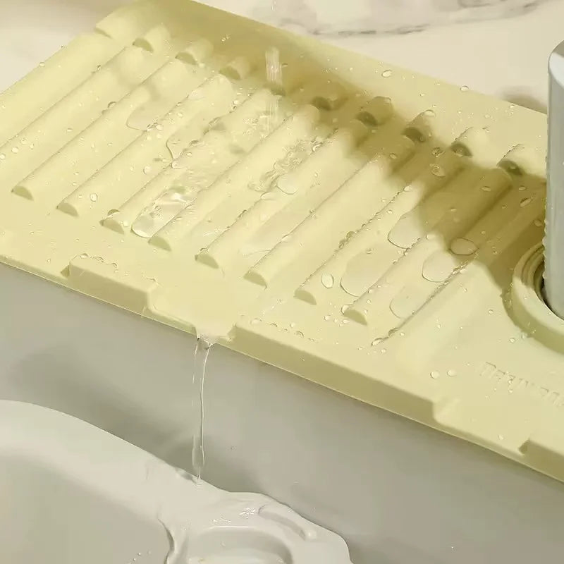 A light yellow silicone mat with grooves is shown dripping water into a white sink.