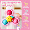 A pink suction cup spinner sensory toy with colorful parts is shown being played with by a hand.
