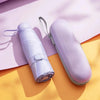 A light purple compact 5-fold travel umbrella with a strap is shown on a yellow background.