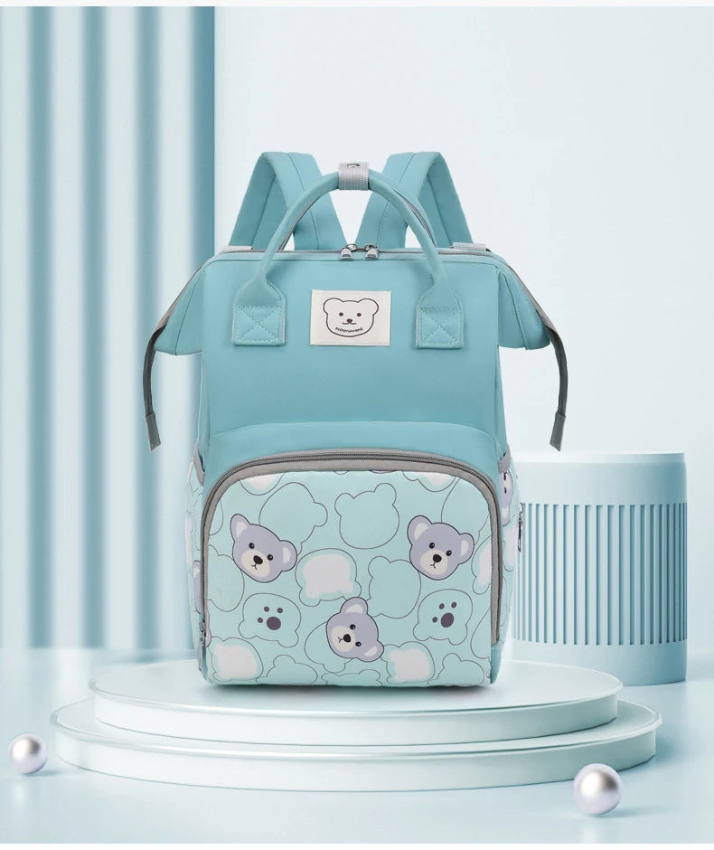 A light blue bear print waterproof diaper backpack displayed on a white stand against a light blue background.