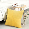 Two yellow corduroy patchwork throw pillows resting on a light gray rug next to a white sofa.