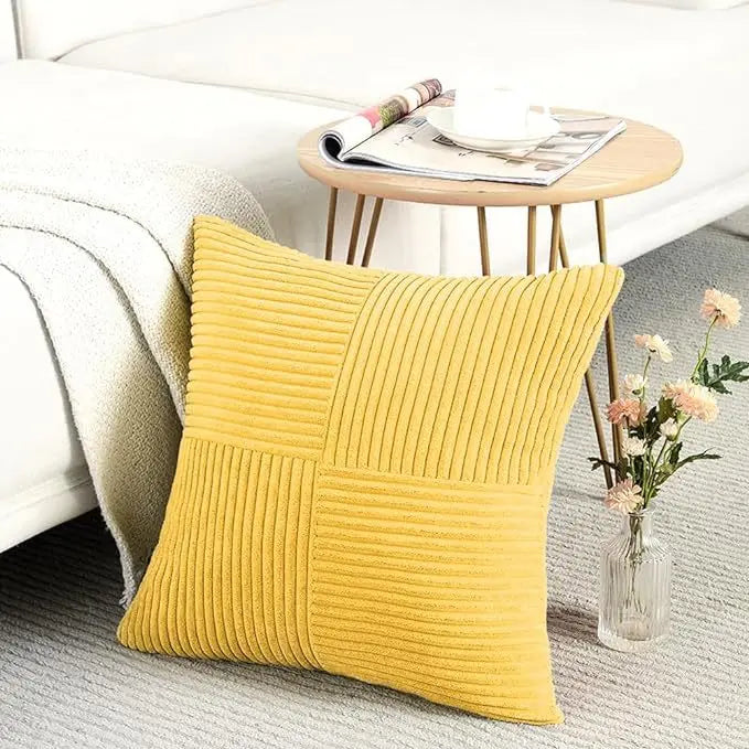 Two yellow corduroy patchwork throw pillows resting on a light gray rug next to a white sofa.