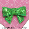 A bright green sequin bow patch is shown against a pink grid background.
