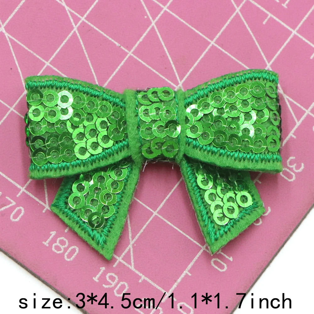 A bright green sequin bow patch is shown against a pink grid background.