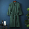 A dark green lightweight cotton waffle robe hanging on a wall against a dark blue background.