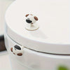 A white cartoon dog-shaped toilet seat lifter handle is visible on a white toilet bowl.