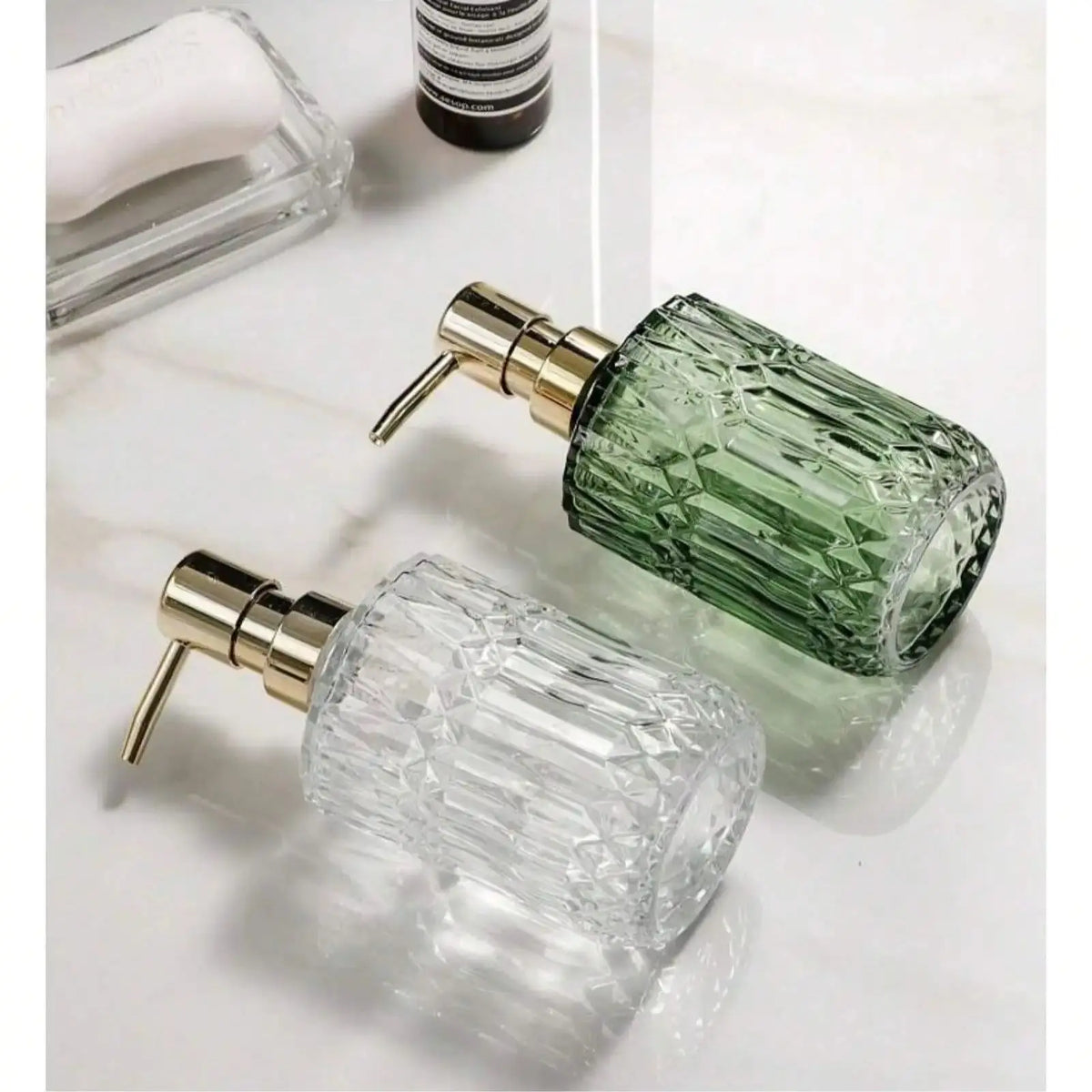 A clear glass soap dispenser with a gold pump mechanism and a green liquid refill bottle.